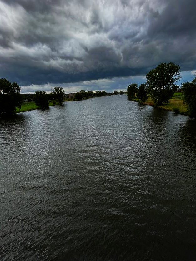 Foto van de Maas met een donkere wolk erboven.  